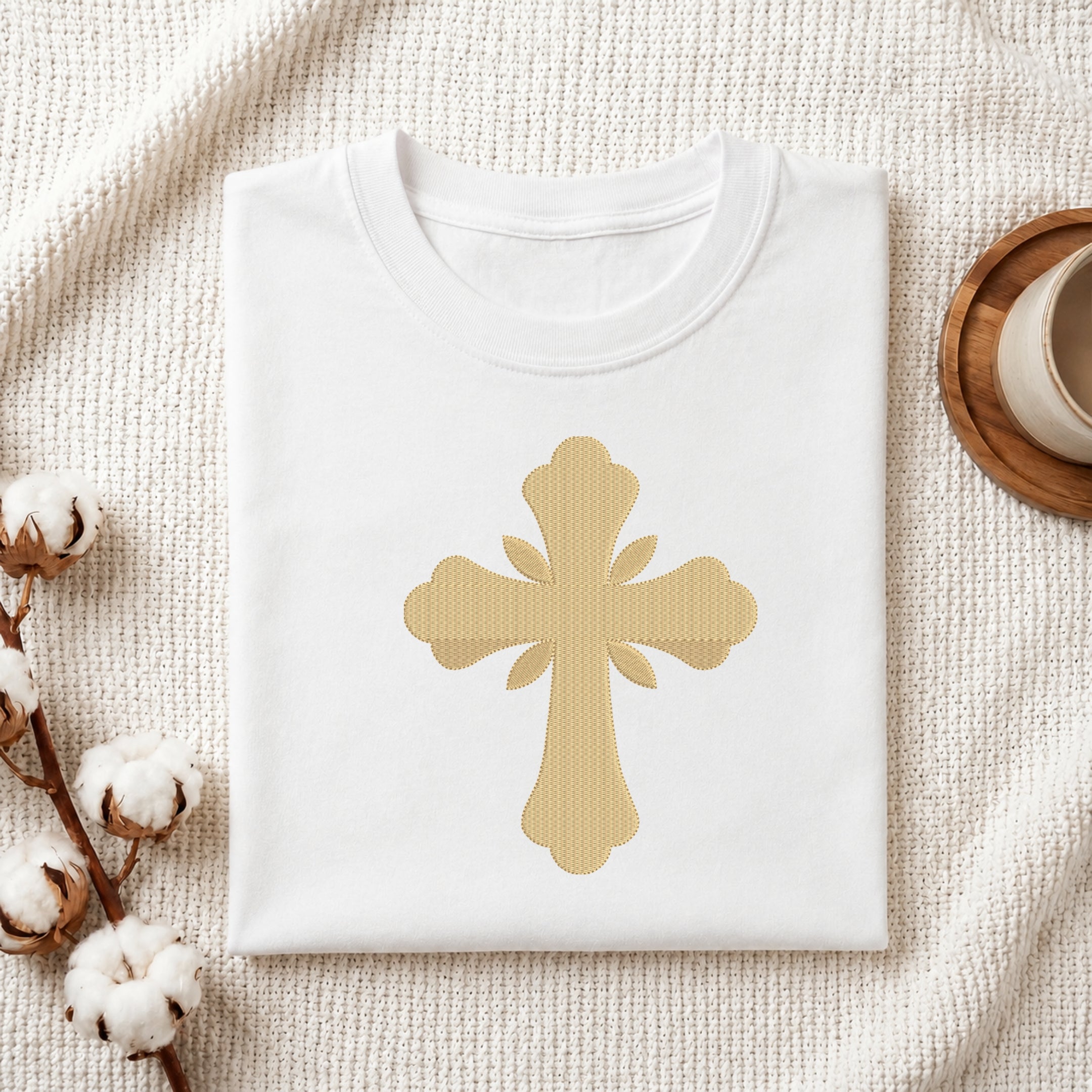 Folded white cotton t-shirt featuring a golden ornamental cross embroidery design centered on the chest.