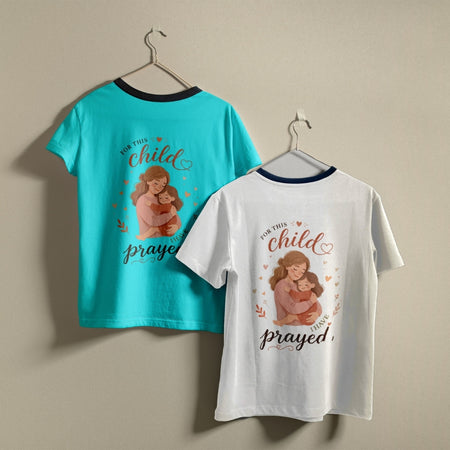 Two t-shirts hanging on hangers, one purple and one white, both printed with a mother-and-child illustration and the text "For this child I have prayed."