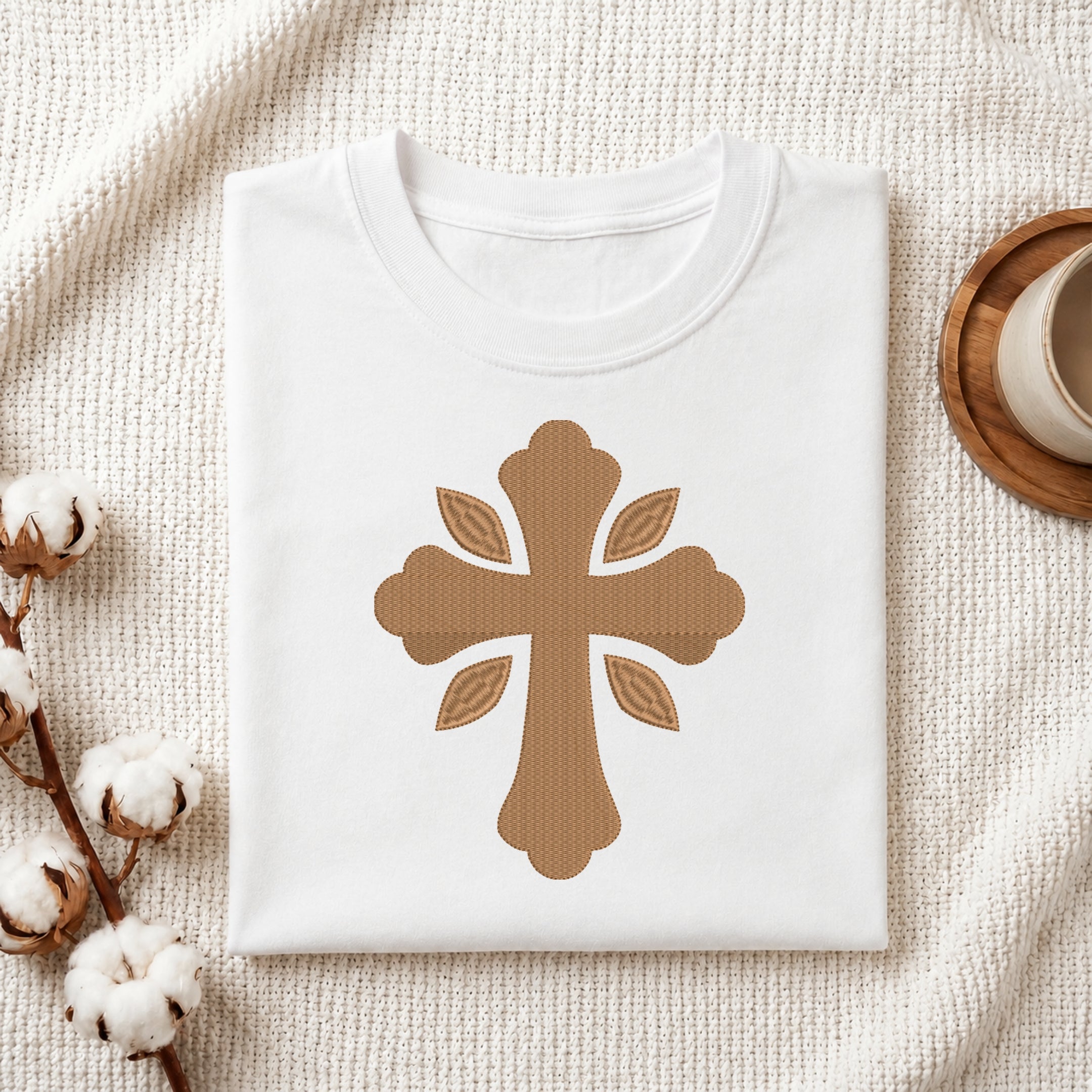 Folded white cotton t-shirt featuring a golden leaf cross embroidery design centered on the chest.