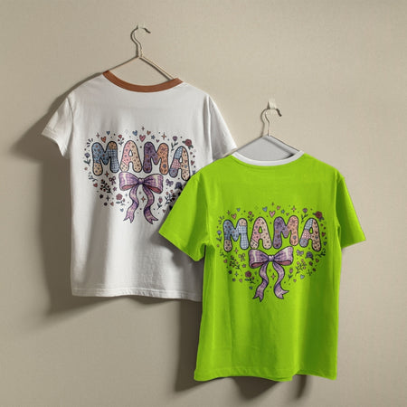 Two children's short-sleeve T-shirts hanging on hangers against a plain beige wall. The left shirt is white with a brown collar trim and a colorful 'MAMA' heart graphic on the back.