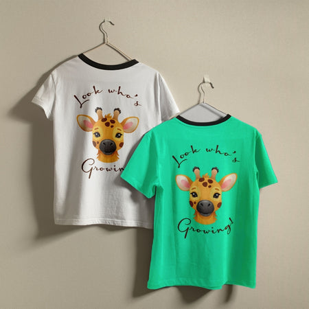 Two crewneck t-shirts, one white and one bright green, hanging on a wall showing the cute giraffe Look Whos Growing graphic design.