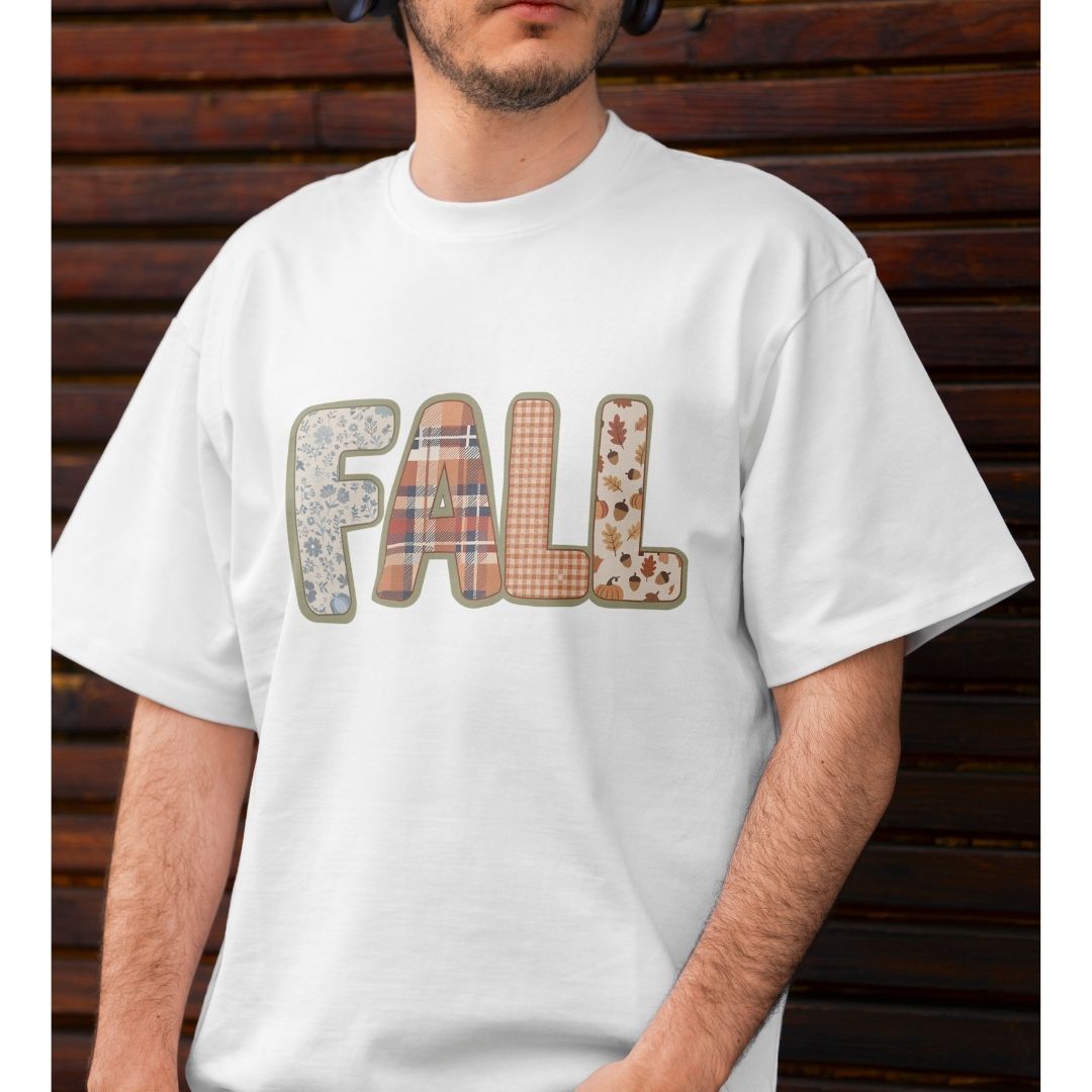 A man wearing a white crewneck t-shirt with the word 'FALL' printed across the chest in decorative autumn-themed patterned letters, posed against a dark wooden slat background.