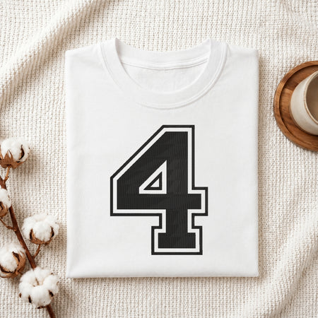 A folded white t-shirt with a large black number 4 outlined in white on the front, styled on a textured cream fabric with cotton bolls and a wooden cup.