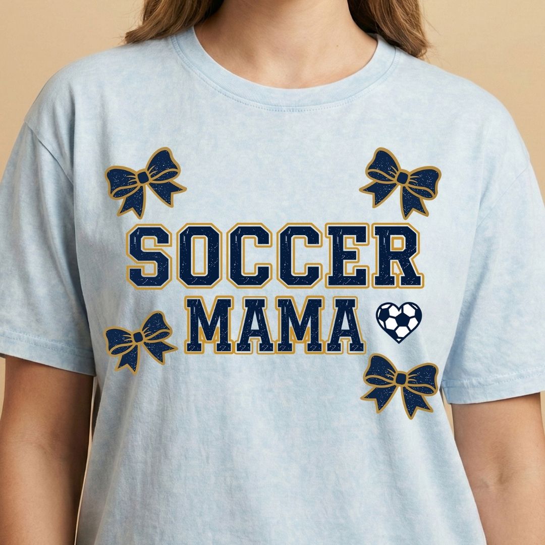 Light blue t-shirt with 'Soccer Mama' text and decorative elements on a beige background