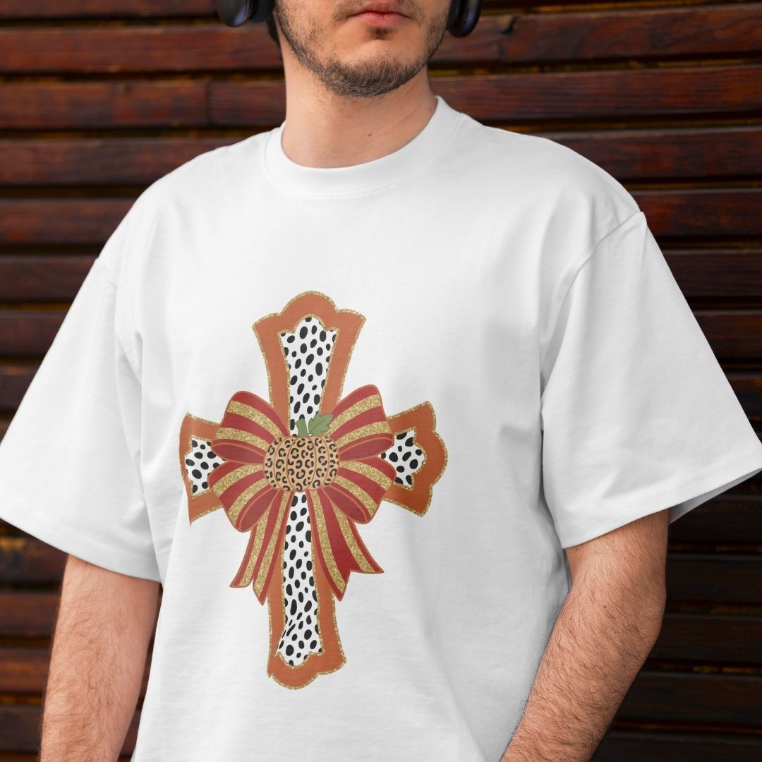 A man wearing a white crewneck t-shirt with a large decorative cross graphic on the front. The graphic features a brown and gold ribbon bow design with black-and-white spotted leopard print details.