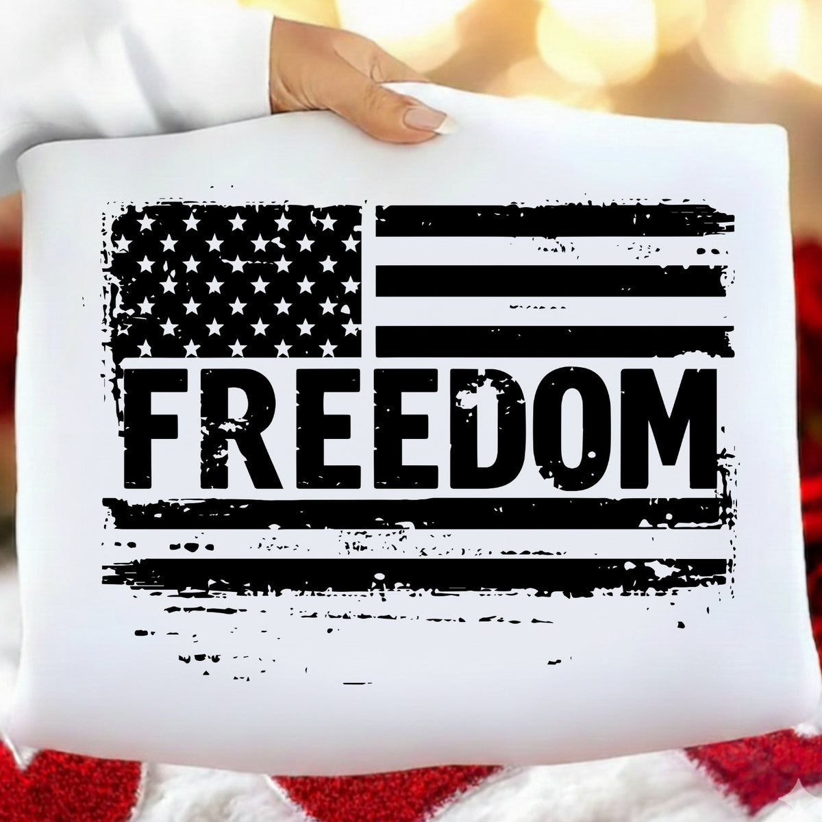 White pillow with American flag and 'FREEDOM' text held by a person against a blurred background