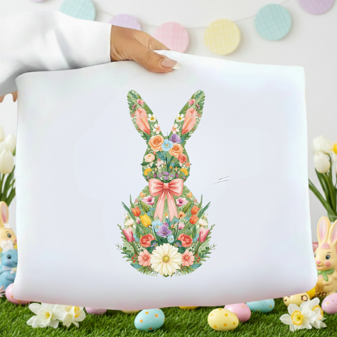Decorative pillow with floral bunny design held by a hand, surrounded by Easter decorations.