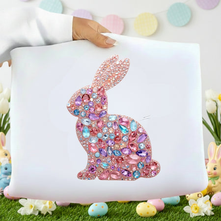 Decorative pillow with a jeweled bunny design on a white background, surrounded by Easter decorations.