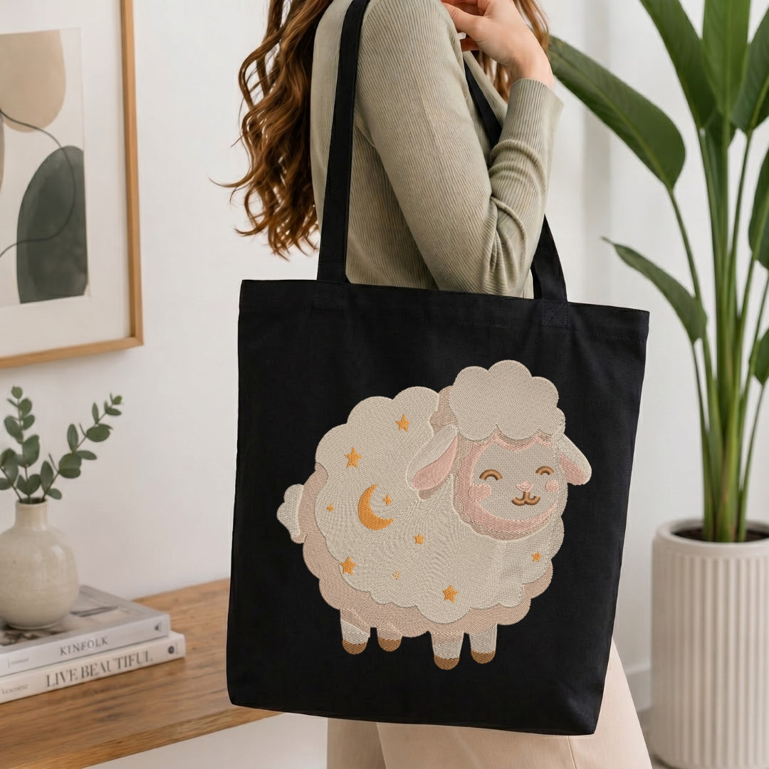 A person wearing a beige ribbed sweater carries a black canvas tote bag with a large embroidered sheep design in cream, pink, and yellow. The setting is a bright, modern room with a wooden table, books, a framed print, and a potted plant.