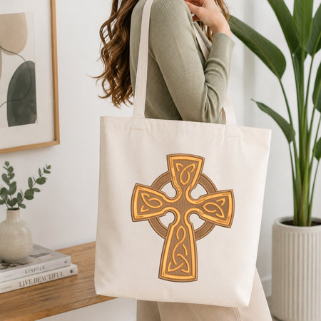 Woman holding a beige canvas tote bag customized with a detailed Celtic cross embroidery pattern.