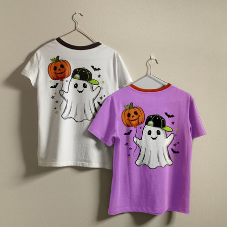 Two children's short-sleeve t-shirts with a Halloween ghost and pumpkin graphic, hanging on hangers against a beige wall. One shirt is white with a dark brown collar, and the other is purple with an orange collar.