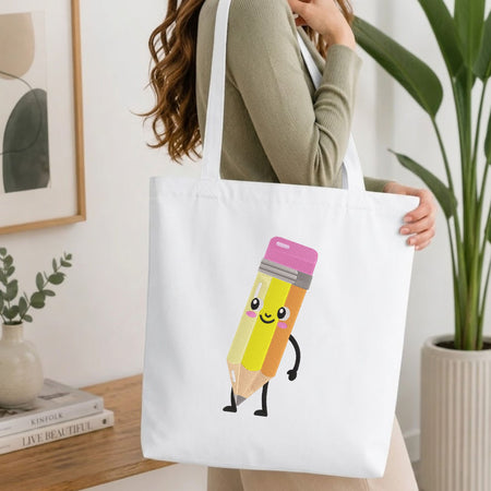 A woman wearing a sage green ribbed long-sleeve top carries a white canvas tote bag. The bag features a cute cartoon graphic of a smiling yellow pencil with a pink eraser cap and black limbs.