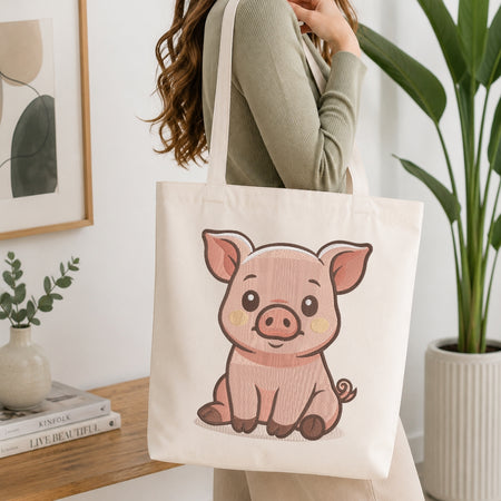 A woman wearing a sage green ribbed sweater carries a cream canvas tote bag featuring a cute pink cartoon pig illustration. The scene is set in a bright, modern room with a wooden table, books, a small vase, and a potted plant.