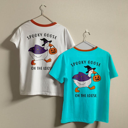 Two crewneck t-shirts in white and bright turquoise hanging on hangers against a wall, both featuring the back-printed Spooky Goose Halloween graphic.