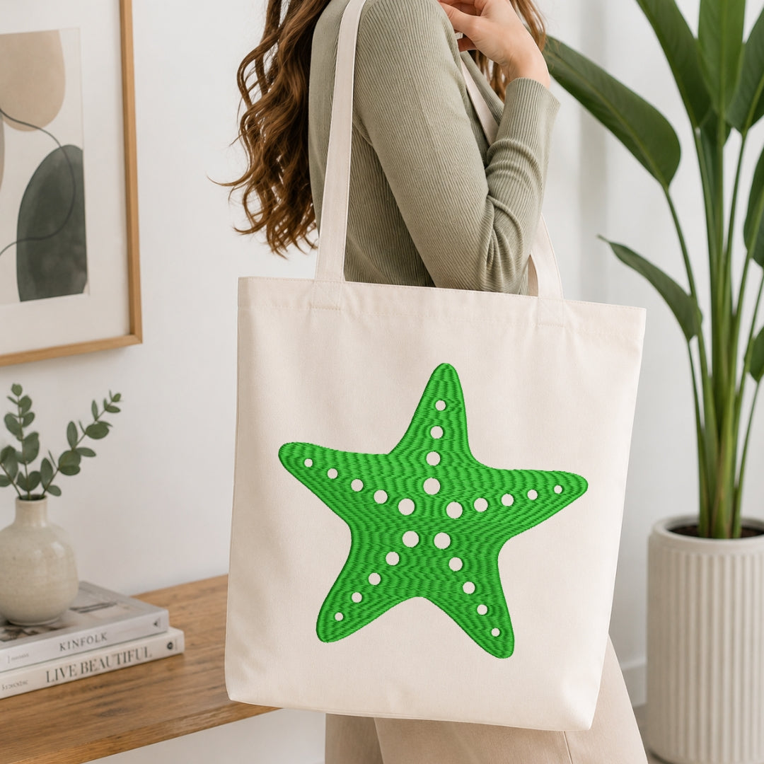 An off-white canvas tote bag with a large green starfish applique on the front, carried by a woman in a ribbed sage green top in a bright, modern room.