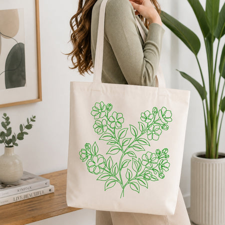 A person is shown carrying a cream-colored canvas tote bag that features the same green, line-art floral embroidery design.