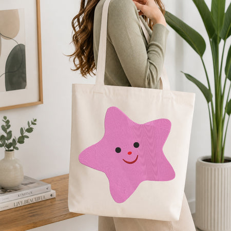 Person carrying a canvas tote bag featuring the stitched pink star design.