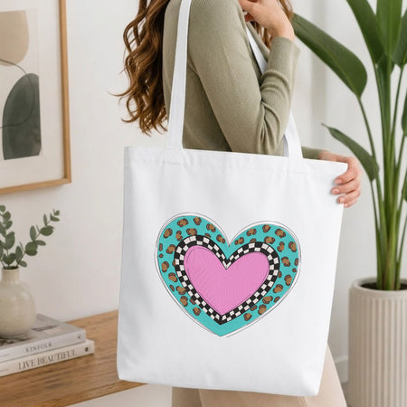 Woman carrying a white natural canvas tote bag featuring a layered leopard heart machine embroidery design in a bright, modern interior setting