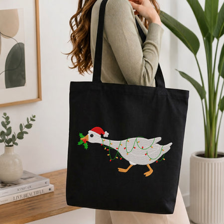 Woman carrying a black canvas tote bag with a festive embroidered Christmas goose.
