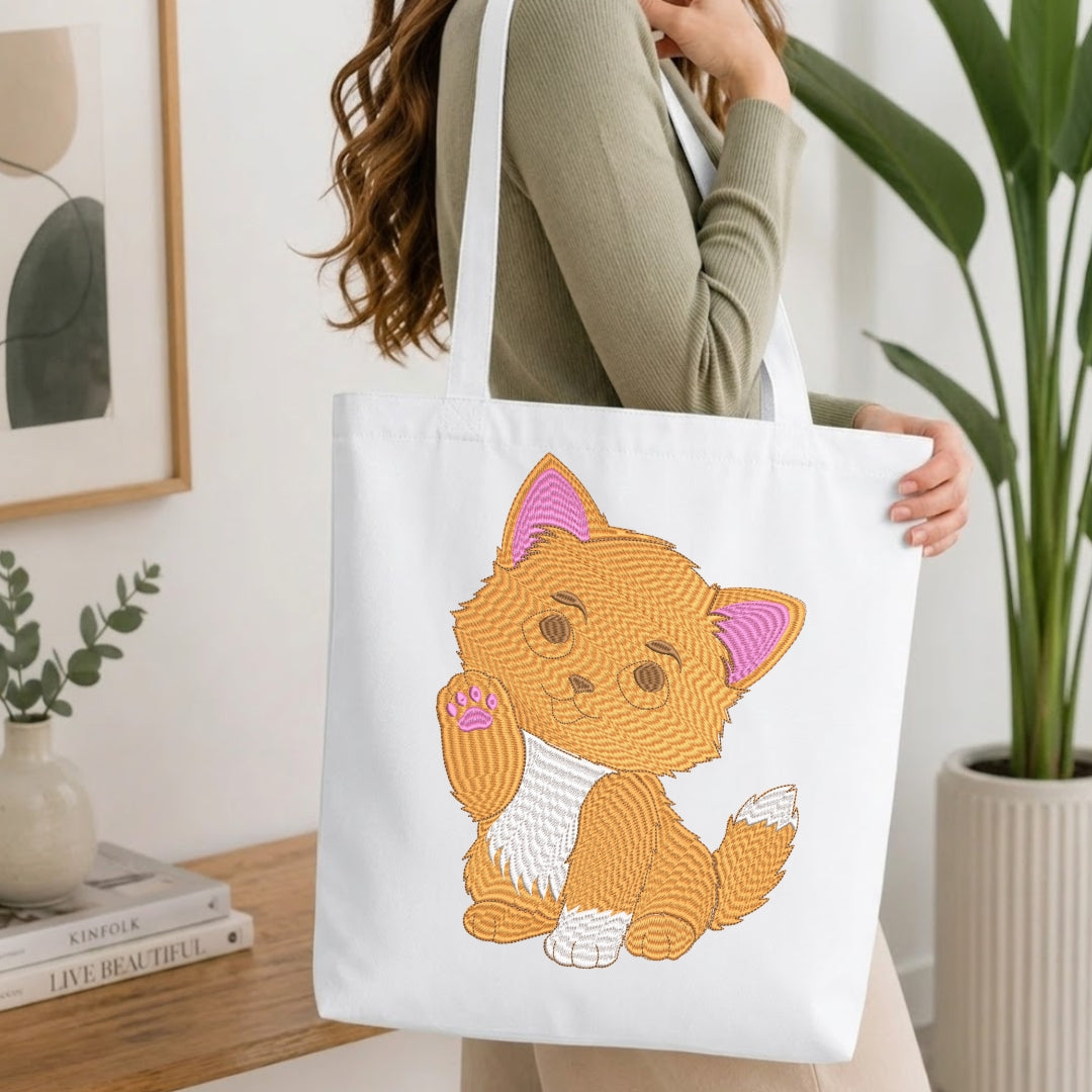 A person carrying a cream-colored canvas tote bag decorated with the embroidered orange kitten design.