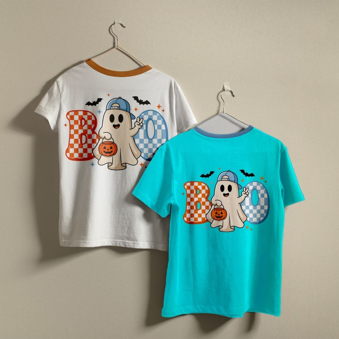 Two t-shirts hanging on a wall—one white and one bright blue—both displaying the cute Halloween ghost and checkerboard "BOO" graphic print.