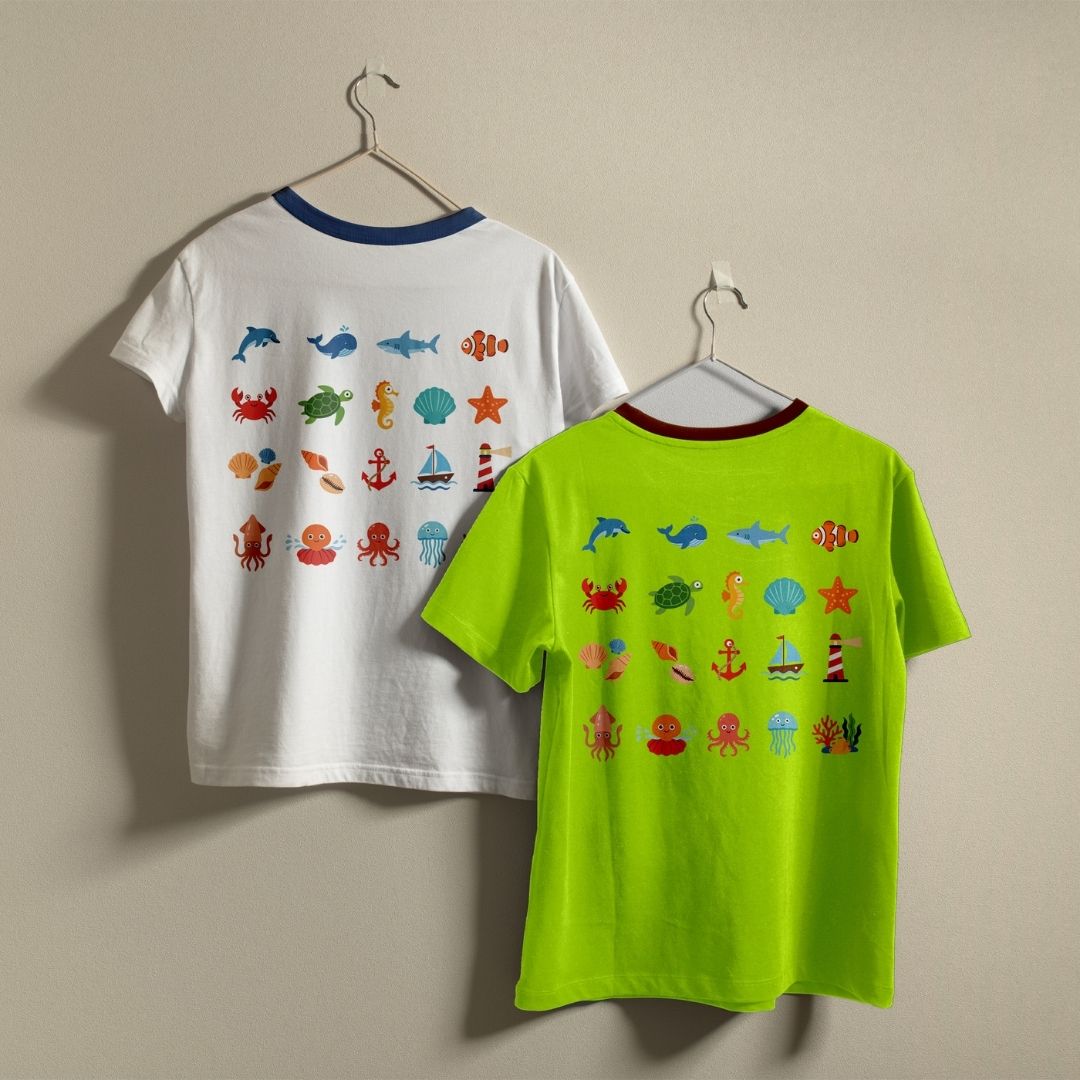 Two children's short-sleeve ringer T-shirts hanging on hangers against a plain beige wall. The left shirt is white with a navy collar and colorful ocean-themed graphics on the back, including fish, crabs, seashells, anchors, and starfish.