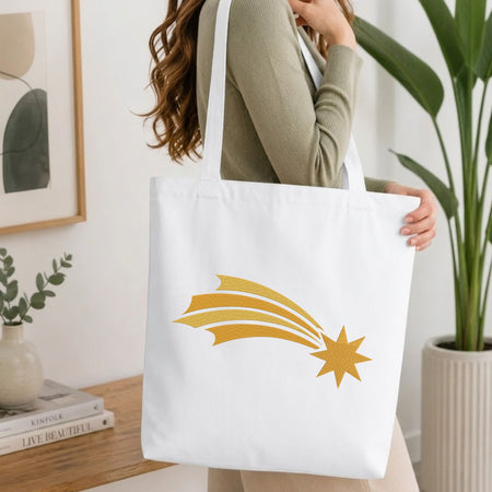 Woman carrying a white natural canvas tote bag featuring an embroidered golden starburst design in a bright, modern interior setting