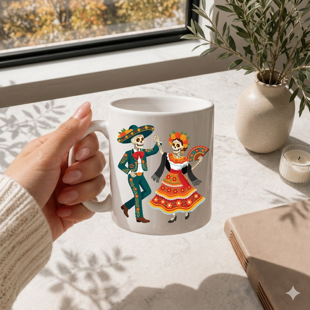 A hand holds a white ceramic mug featuring a colorful Day of the Dead illustration of a dancing skeleton couple, set on a light marble surface near a window with a plant and candle.