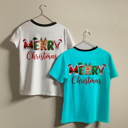 Two t-shirts hanging on a wall—one white and one turquoise—both showcasing the "MERRY Christmas" holiday print design.