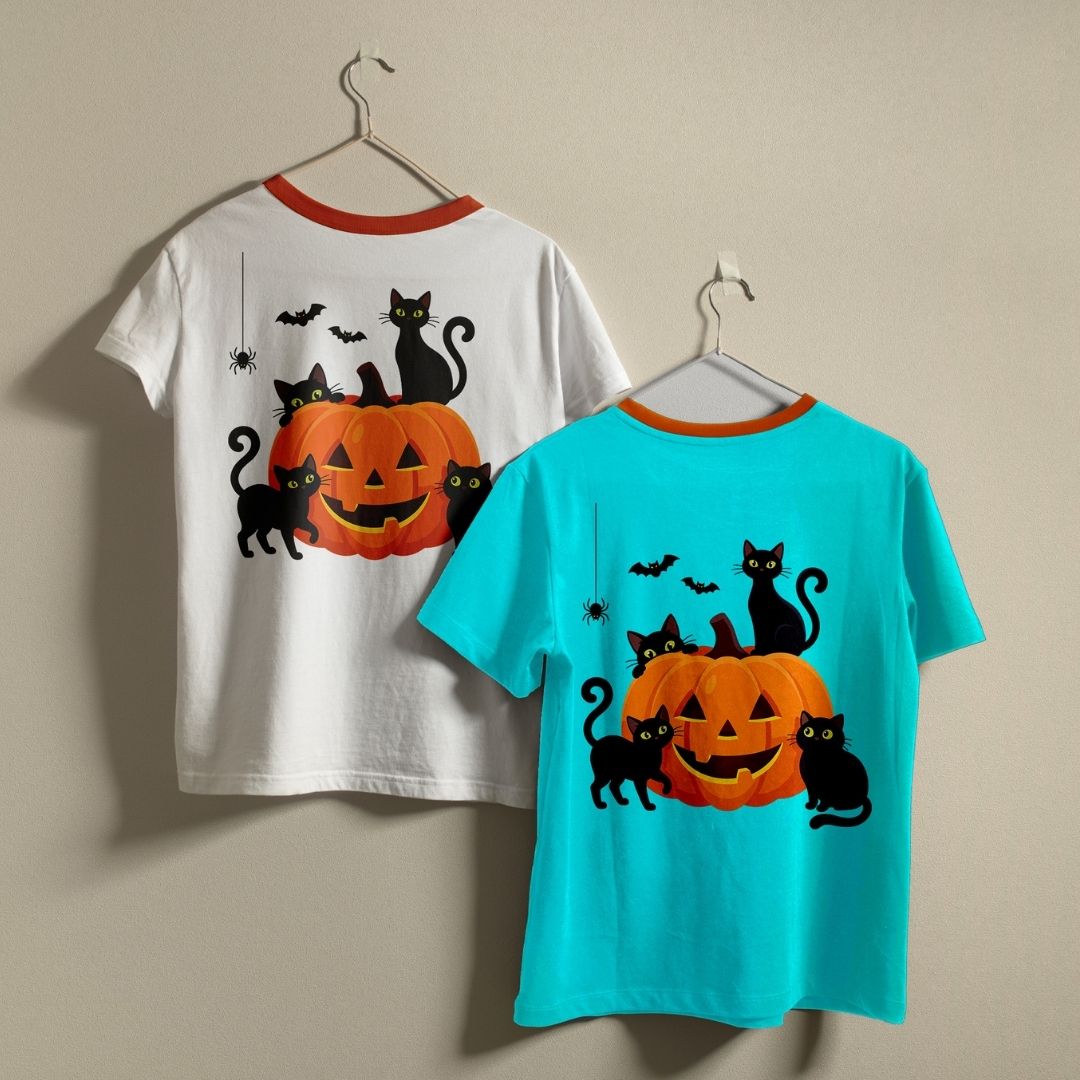 Two t-shirts hanging on a wall—one white and one bright blue—both displaying the cute Halloween black cats and pumpkin graphic print.