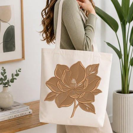 A person carrying a canvas tote bag decorated with the same brown-toned embroidered flower design.