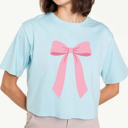 A cropped light blue t-shirt with a large pink bow graphic printed on the front, worn by a model.