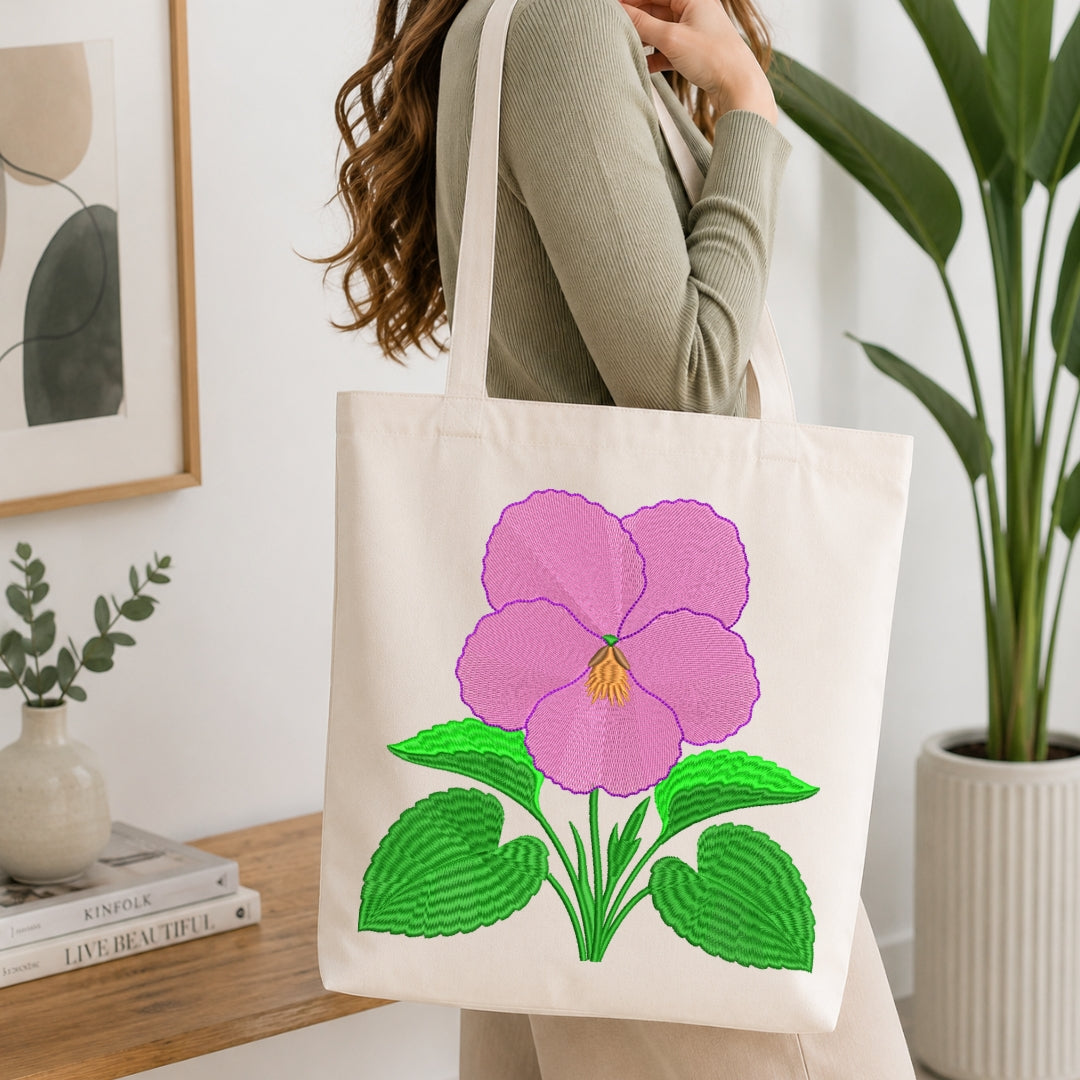 A person carrying a cream-colored canvas tote bag decorated with the pink pansy embroidery design.