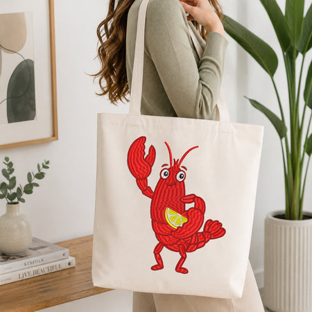 A woman wearing a sage green ribbed sweater carries a cream canvas tote bag with a red cartoon lobster holding a yellow lemon slice, set in a bright, modern room with a wooden table and potted plants.