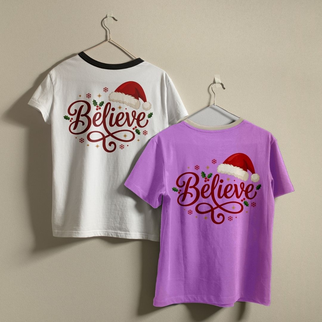 Two crewneck t-shirts in white and purple hanging on a wall, both featuring a red "Believe" Christmas design.