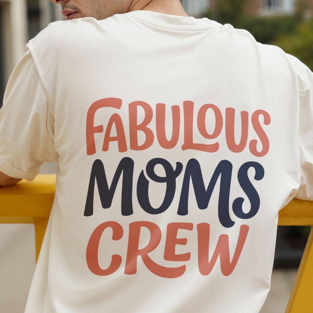 Back view of a person wearing an off-white t-shirt featuring the typography graphic "FABULOUS MOMS CREW" printed large on the upper back in coral pink and navy blue lettering.