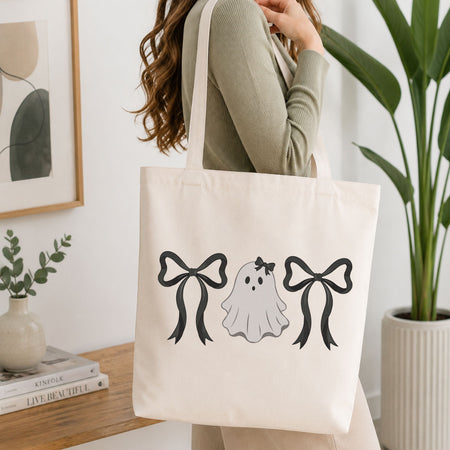 Woman carrying a white natural canvas tote bag featuring a cute ghost with bows machine embroidery design in a bright, modern interior setting   