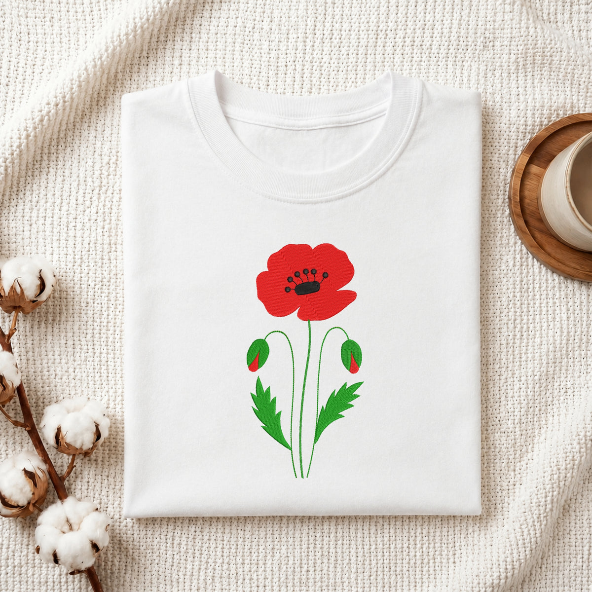Folded white t-shirt featuring a red poppy flower embroidery design centered on the chest.