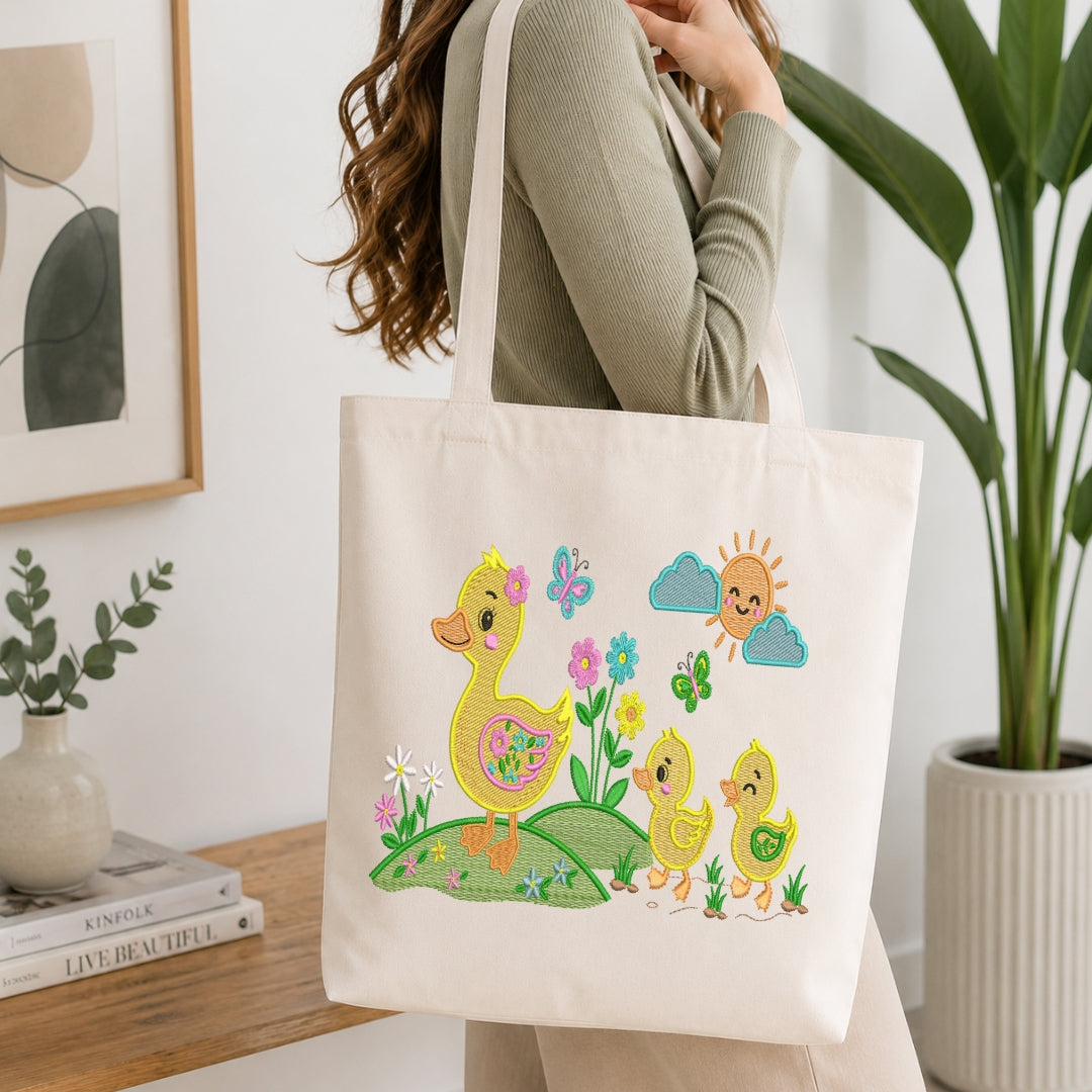 An off-white canvas tote bag with a colorful Easter-themed duck illustration, carried on the shoulder of a person in a ribbed sage green top, set against a bright, modern indoor background with a potted plant and framed art.