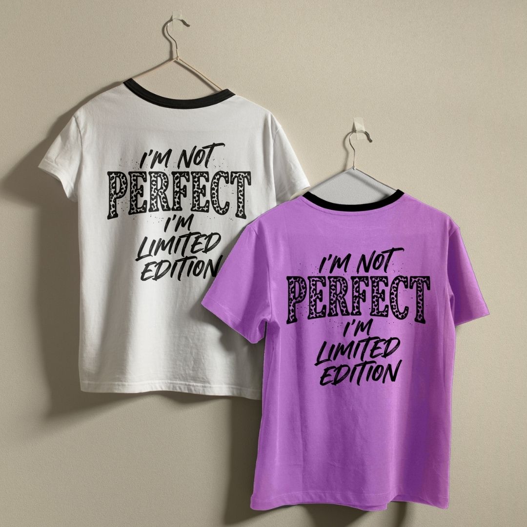 Two ringer t-shirts hanging on hangers against a plain beige wall. The left shirt is white with black trim and black graphic text reading 'I'M NOT PERFECT I'M LIMITED EDITION'.