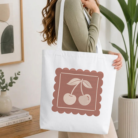 Woman carrying a white natural canvas tote bag featuring an embroidered vintage cherry design in a bright, modern interior setting.   