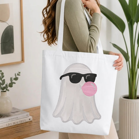 Person carrying a canvas tote bag featuring the stitched cool ghost design