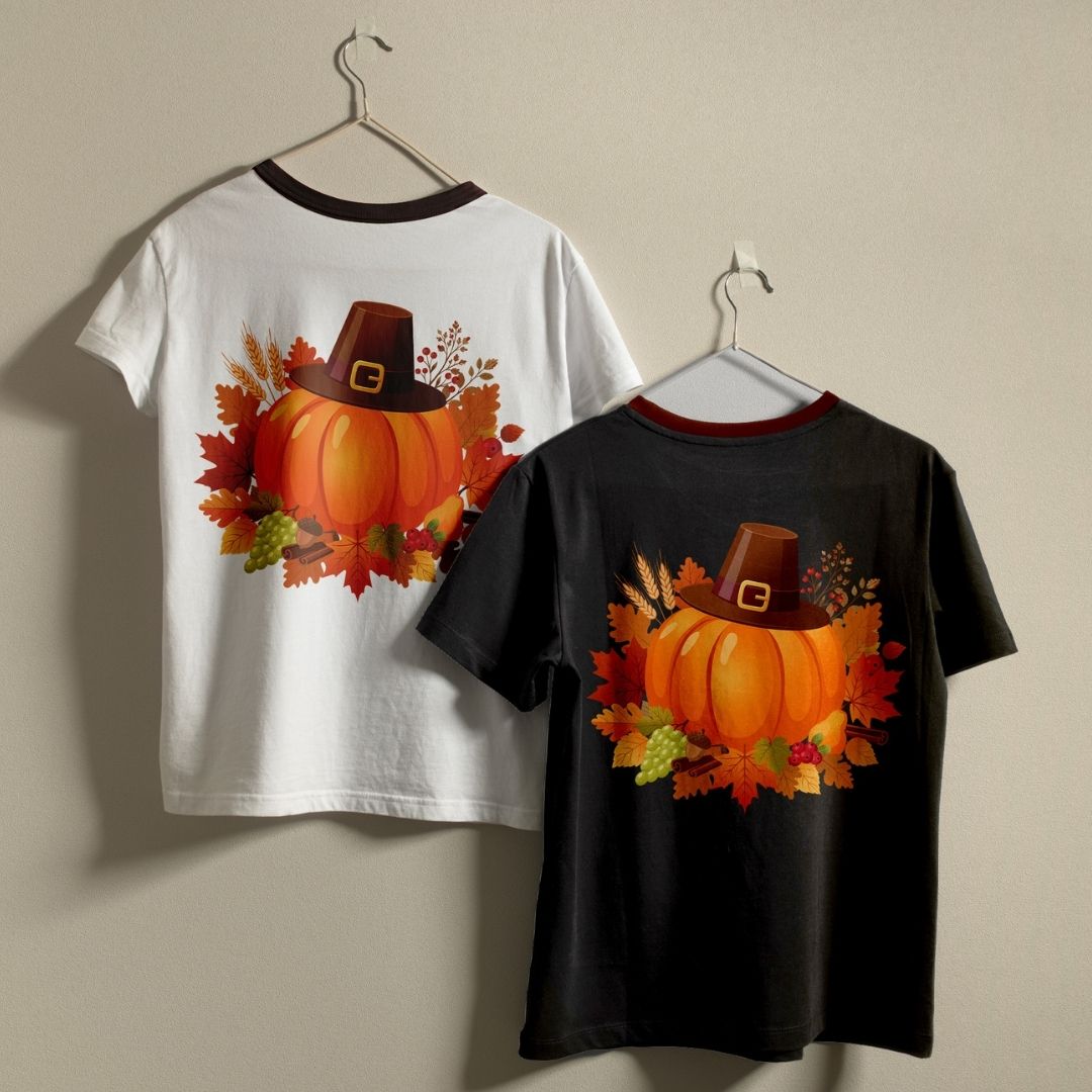 Two kids' short-sleeve ringer t-shirts hanging on hangers against a plain beige wall. The left shirt is white with a dark collar and features a back graphic of an orange pumpkin wearing a brown pilgrim hat surrounded by autumn leaves.