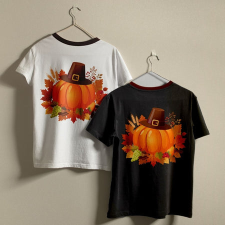 Two kids' short-sleeve ringer t-shirts hanging on hangers against a plain beige wall. The left shirt is white with a dark collar and features a back graphic of an orange pumpkin wearing a brown pilgrim hat surrounded by autumn leaves.