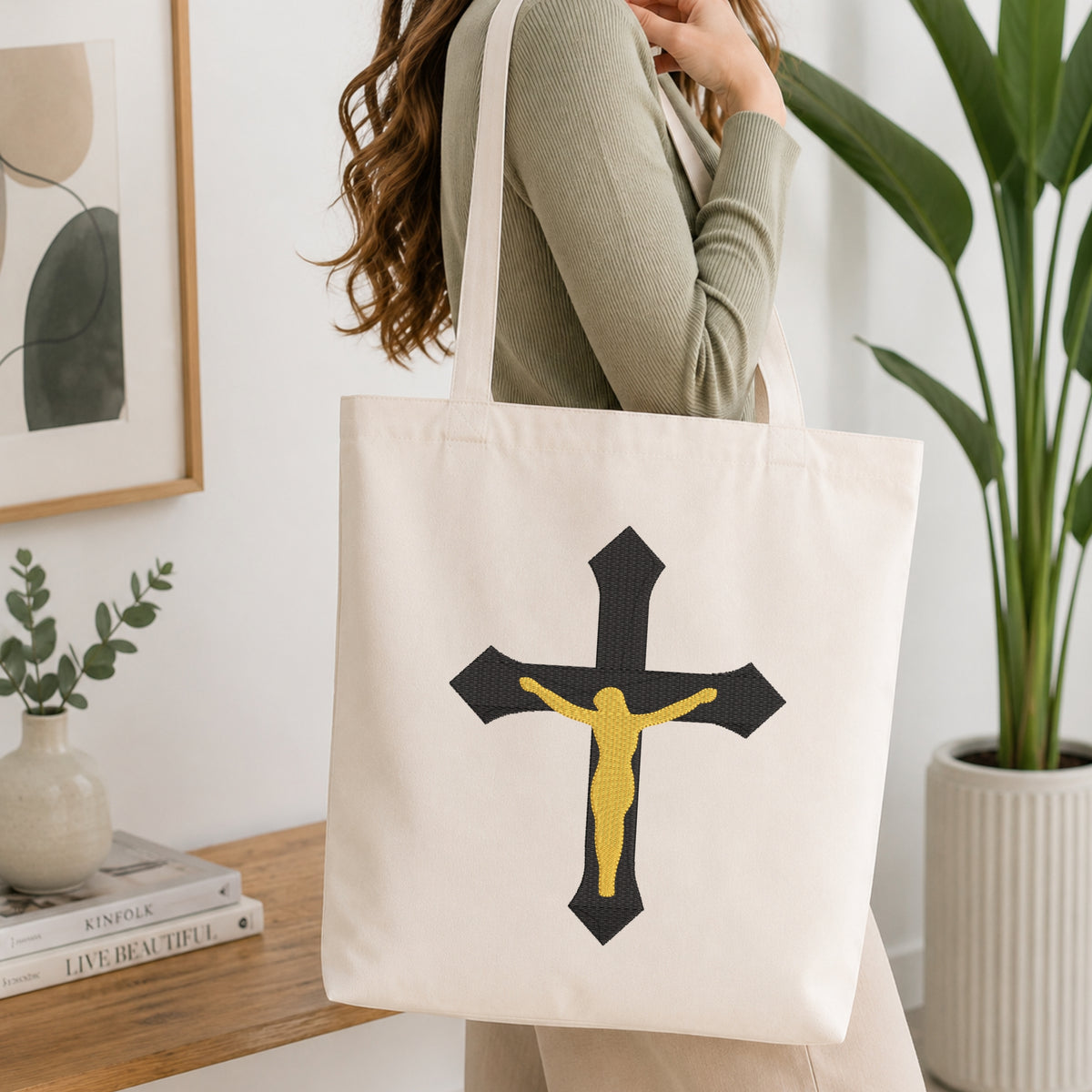 Woman carrying a beige canvas tote bag customized with a black and gold crucifix embroidery design.