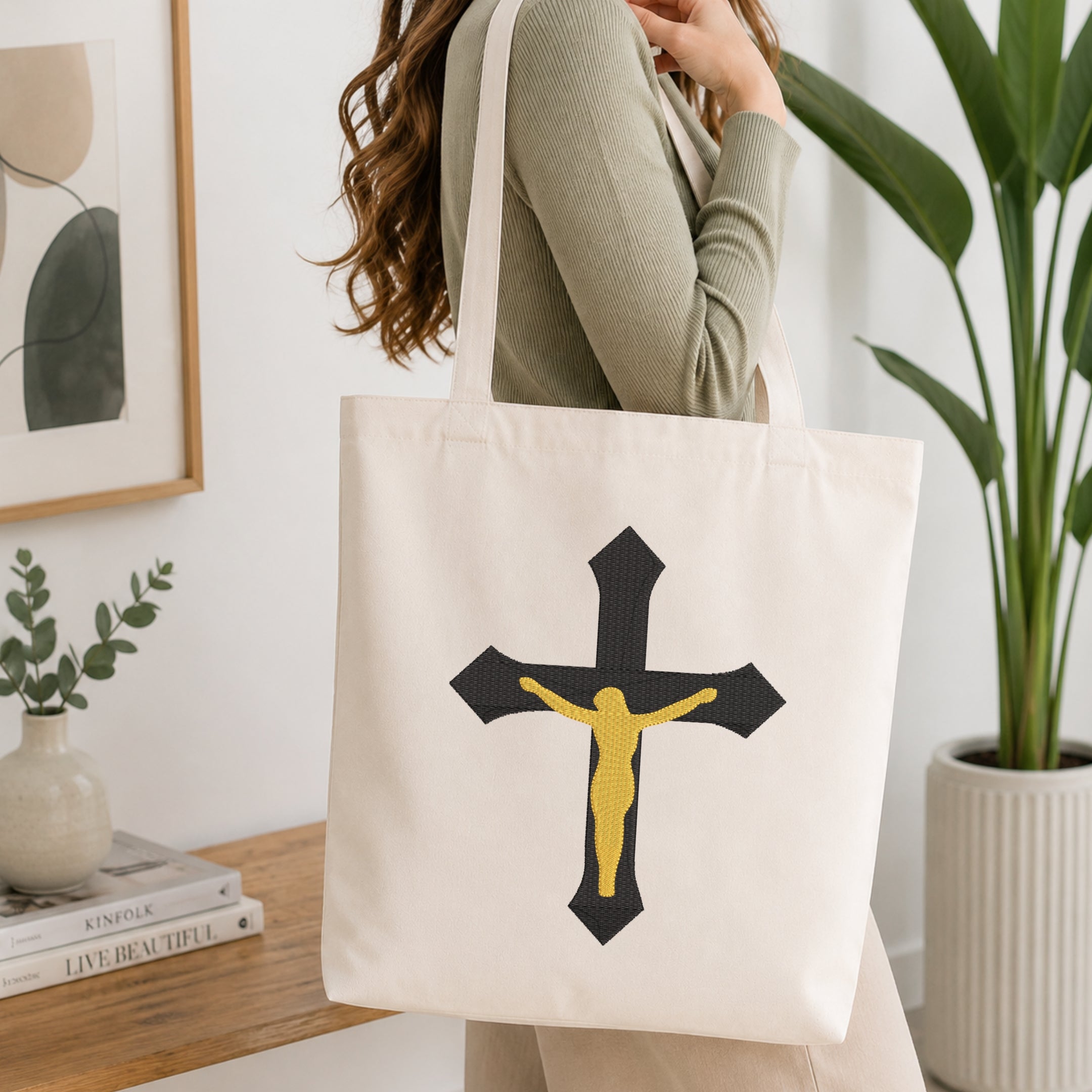 Woman carrying a beige canvas tote bag customized with a black and gold crucifix embroidery design.