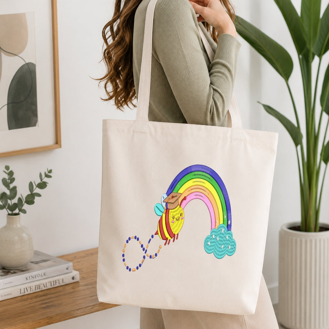A woman wearing a ribbed sage green long-sleeve top carries a cream canvas tote bag. The bag features a colorful embroidered design of a rainbow arching over a yellow sun and a blue cloud, with a beaded line connecting them.