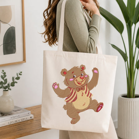 A person carrying a cream-colored tote bag showcasing an embroidered dancing bear design.