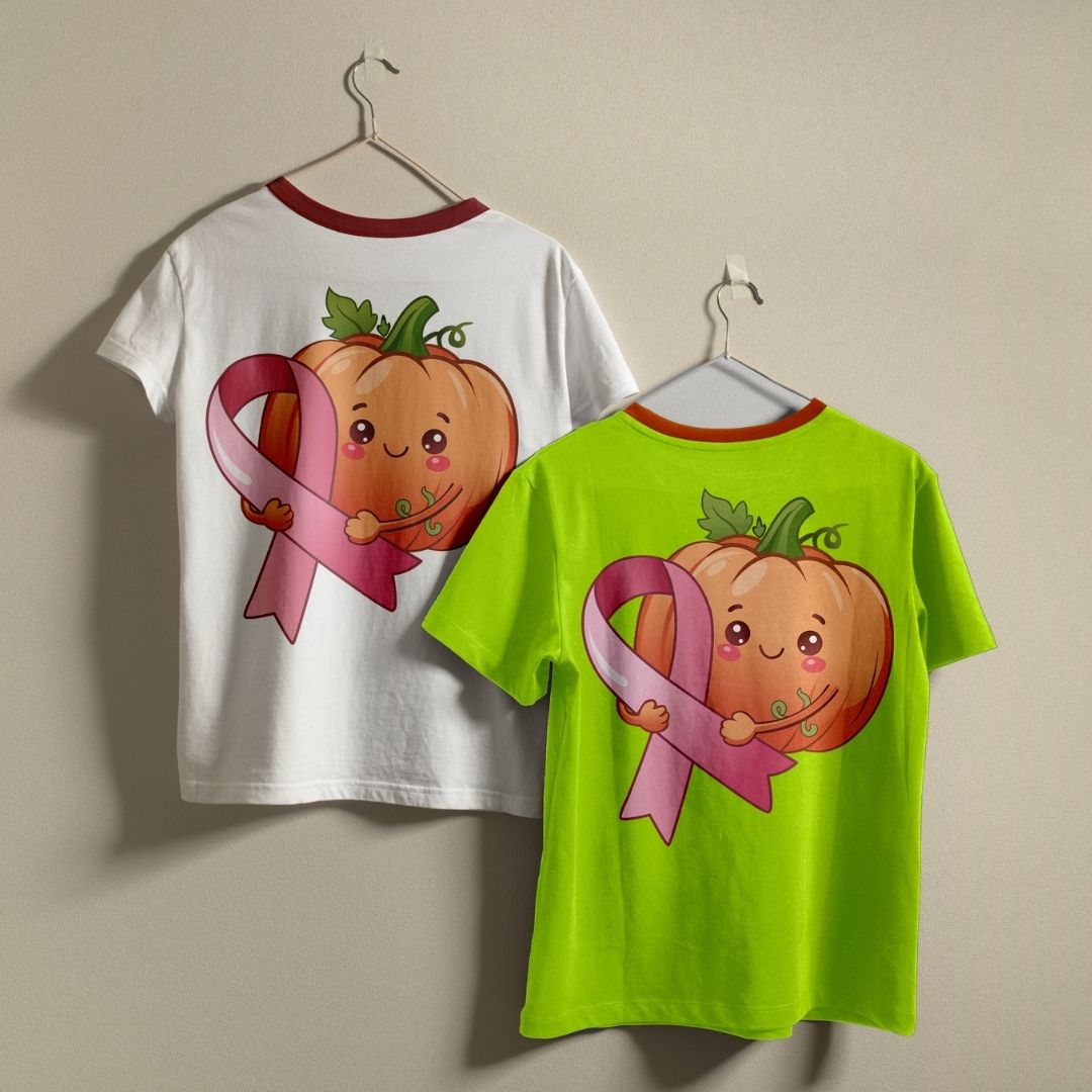 Two ringer t-shirts on hangers, one white and one neon green, both featuring a graphic of a smiling cartoon pumpkin holding a pink ribbon on the back.