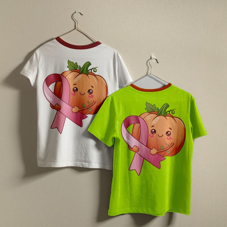 Two ringer t-shirts on hangers, one white and one neon green, both featuring a graphic of a smiling cartoon pumpkin holding a pink ribbon on the back.